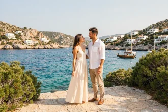 Couple romantique sur un ponton en pierre à Porto Cervo en Sardaigne, avec vue sur les eaux turquoise de la Méditerranée et les villas blanches sur les collines granitiques