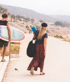 man holding surfboard while walking with woman