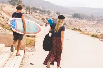 man holding surfboard while walking with woman